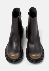 Botas negras de cuero hasta el tobillo con acabado brillante, con puntera redondeada, cap toe marrón en contraste y suela de goma texturizada.