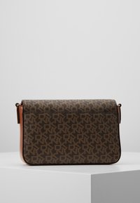 Brun rektangulär handväska med mörkbrunt monogrammönster och beige läderdetaljer, ställd på en vit pelare mot en neutral bakgrund.