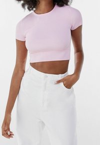 Světle růžový žebrovaný crop top s krátkými rukávy, sladěný s bílými džíny s vysokým pasem. Top má kulatý výstřih a přiléhavý střih.