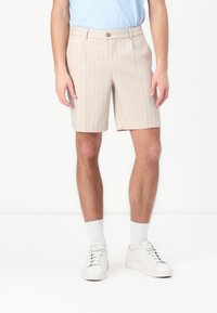 Beige pinstriped shorts made of lightweight fabric, featuring a button closure and side pockets, paired with white sneakers and socks.