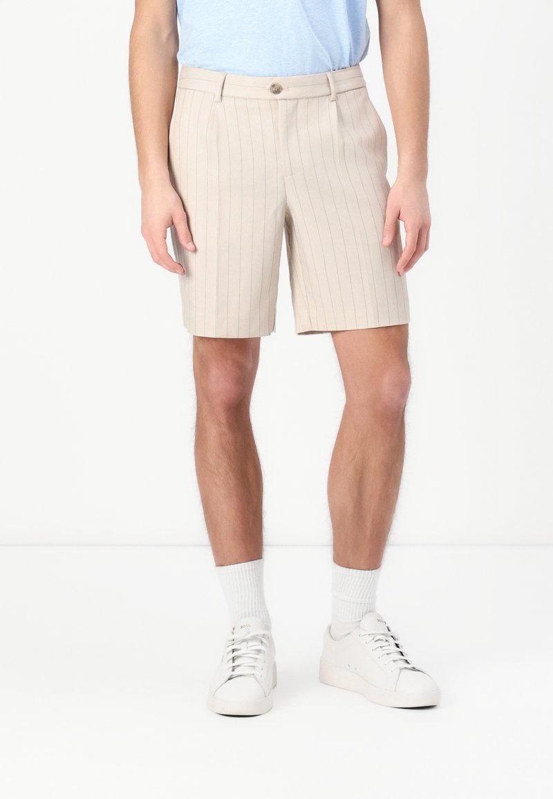 Beige pinstriped shorts made of lightweight fabric, featuring a button closure and side pockets, paired with white sneakers and socks.