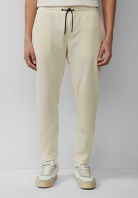 Lichtcrème joggers met een trekkoord in de taille, taps toelopende broekspijpen en twee zijzakken, gecombineerd met witte en grijze sneakers.