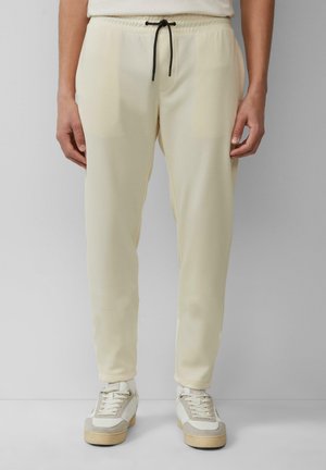 Lichtcrème joggers met een trekkoord in de taille, taps toelopende broekspijpen en twee zijzakken, gecombineerd met witte en grijze sneakers.