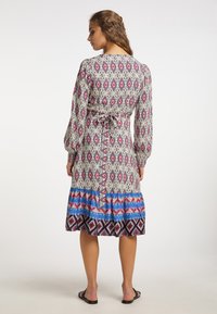 Rochie cu mânecă lungă, cu un imprimeu geometric multicolor, talie strânsă cu o panglică și fustă cu volane cu modele albastre și roșii.