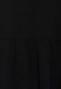 Svart kl änning med samlad midja, tillverkad av lättviktigt tyg med texturerad yta. Nederkanten faller strax under midjan.