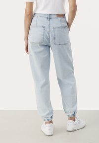 Jasnoniebieskie dżinsowe joggery o luźnym kroju, z elastycznymi mankietami i dwoma tylnymi kieszeniami, zestawione z białymi trampkami.