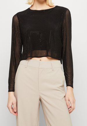 Czarny prześwitujący crop top z długim rękawem i małymi kwadratowymi ozdobami, zestawiony z beżowymi spodniami z wysokim stanem.