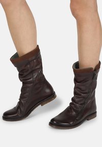 Brown leather ankle boots with a slouchy design, featuring a zip closure, suede cuff, and a flat sole. Textured finish and contrasting interior.