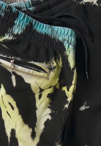 Crne i žute kratke hlače s tie-dye uzorkom, tirkiznom elastičnom trakom u struku, crnim vezicama i džepom na stražnjoj strani sa zatvaračem.