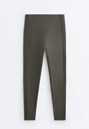 Sötét olívazöld derékban magasított leggings, oldalsó varrással, egyenes szárakkal, látható logók vagy minták nélkül.