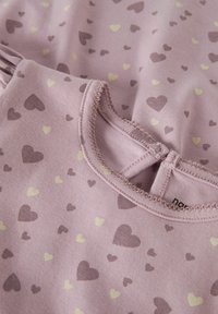 Gros plan sur un tissu rose avec de petits motifs cœurs violet et jaune, et un col rond cousu.