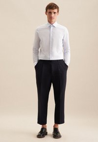 Camicia a righe celesti con colletto a punta, design aderente. Abbinata a pantaloni a pieghe blu scuro e scarpe stringate nere.
