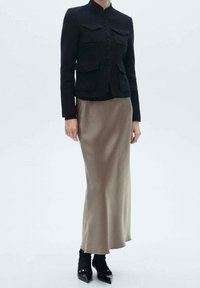 Zwarte wollen blend fitted jack met vier opgestikte zakken en knoopsluiting, gecombineerd met een beige satijnen maxi rok, afgewerkt met puntige zwarte schoenen.