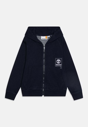 Haut de hoodie zippé navy en coton avec une poche avant, arborant un patch logo Timberland blanc sur la poitrine gauche et des poignets côtelés.