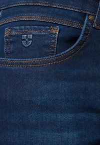 Kieszonka w dżinsach z pomarańczowym przeszyciem i małym haftowanym emblematem na kieszeni na monety, ukazująca teksturę i detale materiału.