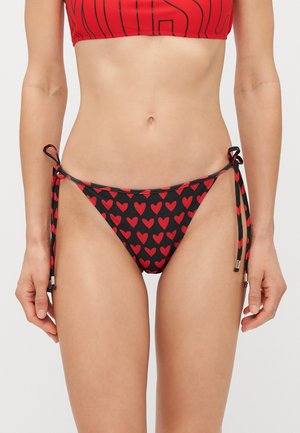 Melns bikinis ar sarkanu sirsniņu rakstu, ar regulējamiem sānu saišu elementiem un metāliskiem akcentiem. Gluda, elastīga auduma.