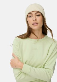 Lichtgroene langarmtop met geribde manchetten, voorzien van subtiele tekstdetails. Witte geribde beanie met een klein zwart logo accent bovenop.