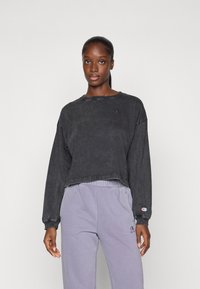 Black cropped sweatshirt in worn look, featuring long sleeves and a small logo on the chest. Paired with light purple sweatpants.