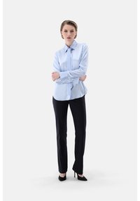 Light blue satin blouse with a collar and neck tie, paired with black tailored trousers and black pointed-toe heels. Simple, sleek design.