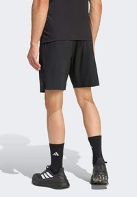 Pantalones cortos deportivos negros hechos de material ligero, con un ajuste relajado, combinados con calcetines negros y zapatillas negras con rayas blancas.