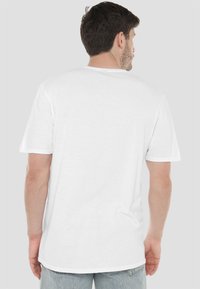 White cotton t-shirt with short sleeves, crew neckline, and a straight hem; displayed from the back against a neutral background.