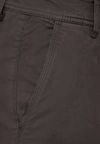 Mörkgrått tyg med en slät textur, med en lätt glans och synliga sömmar längs sömmarna. Nära bild av byxmateriel.