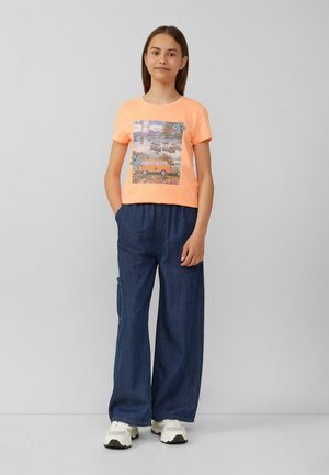 Korte mouwen neon oranje T-shirt met een grafische print van een vintage bus bij water, gecombineerd met losse blauwe spijkerbroek en witte schoenen.