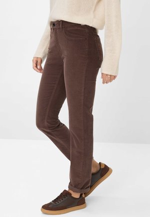 Person wearing brown corduroy pants, beige sweater, and brown sneakers with gum soles, standing against a plain white background.