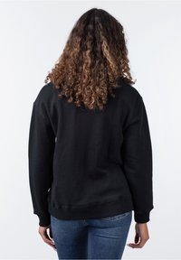 Felpa nera con maniche lunghe, colletto a girocollo e polsini a coste. Il tessuto sembra morbido con una leggera texture. La vista posteriore mostra una vestibilità comoda.