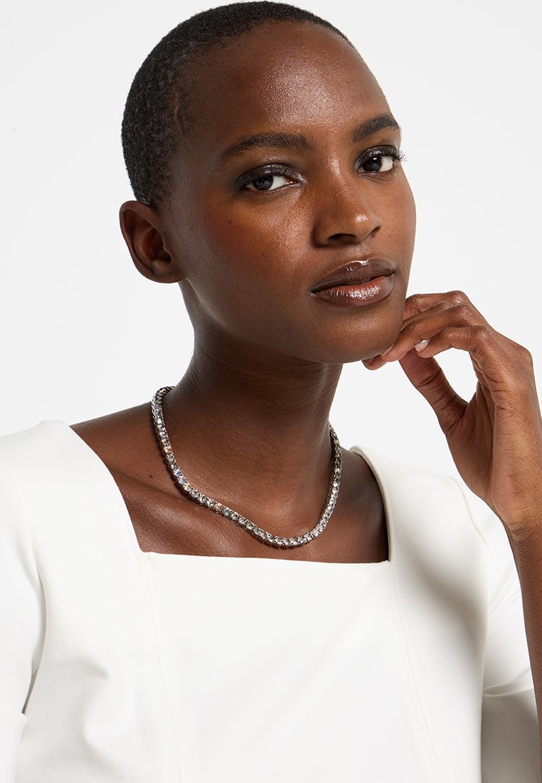 Zilveren ketting met een schakelpunt van heldere edelstenen, gedragen op een witte top met een vierkante halslijn. Glad oppervlak en glanzende afwerking.