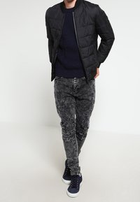 Czarna pikowana kurtka bomber, granatowy sweter dzianinowy, znoszone szare dżinsy i granatowe trampki. Luźny fason o teksturowanym wyglądzie.