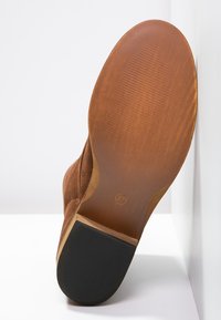 Bottine en daim marron avec une semelle en cuir lisse, un talon arrondi et une semelle extérieure en caoutchouc noir antidérapante. Taille 37 marquée au bas.