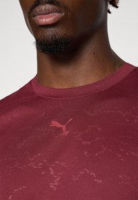 Bordeaux sportshirt met een ronde hals, een gladde textuur en een subtiel patroon, voorzien van een roze Puma-logo op de borst.