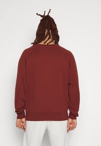 Burgundy sweatshirt med raglanärmar, rund hals och ribbad nederkant. Slät textur och avslappnad passform, lämplig för avslappnad användning.