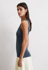 Débardeur sans manches ajusté en tissu côtelé bleu foncé, doté d'un col rond et d'une texture subtile. Associé à une jupe de couleur claire.