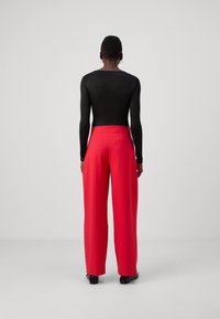 Black long-sleeve bodysuit paired with high-waisted, wide-leg red trousers. Trousers feature a single back pocket and smooth texture.