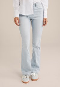 Jeans de campana azul claro fabricados en denim, con una cintura ajustada y botones en la parte delantera. Combinados con zapatillas de deporte de color claro.