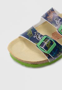 Sandalo blu con accenti verdi, con grafiche di dinosauri. Plantare morbido e testurizzato e suola in sughero. Cinturini regolabili con fibbie in metallo.