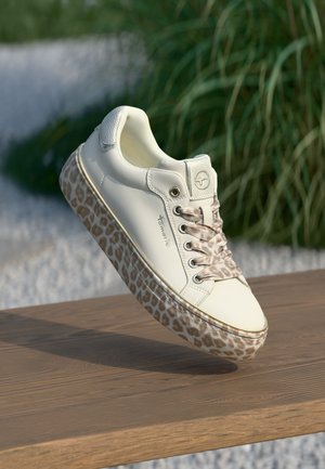 White sneaker with beige leopard print sole and laces, metallic silver heel detail, displayed mid-air above wooden surface outdoors.