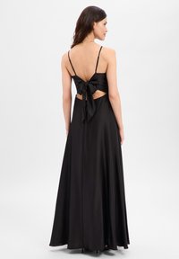 Zwarte satijnen maxi-jurk met een aansluitend lijfje, dunne bandjes en een detail met strik aan de achterkant. Voorzien van uitgesneden zijkanten en een vloeiende rok.