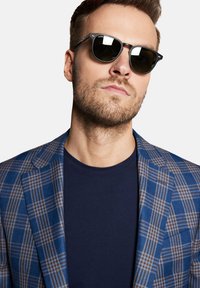 Niebieska i brązowa marynarka w kratkę, noszona na granatowej koszuli, zestawiona z okrągłymi czarnymi okularami przeciwsłonecznymi. Gładki materiał z dopasowanym krojem i kontrastowymi wzorami.
