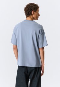 Světle modré bavlněné tričko s volnějším střihem, krátkými rukávy, kulatým výstřihem a spadlými rameny. Jednoduchý design, bez viditelných vzorů nebo akcentů.