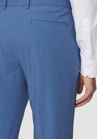 Blaue Anzughose aus leichtem Stoff, mit glatter Textur, schmaler Passform und einer Gesäßtasche. Begleitet von einem weißen Button-Down-Hemd.