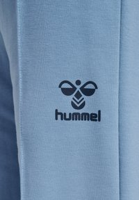 Hellblaue Sporthose aus strukturiertem Stoff mit einem dunkelblauen "hummel"-Logo und einem abstrakten Design im unteren Beinbereich.
