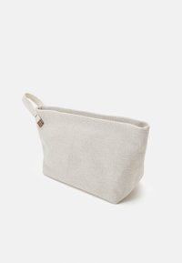 Trousse de toilette rectangulaire beige en tissu avec une anse latérale, présentée sur un fond clair uni.