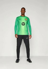 Maillot de gardien à manches longues vert avec des rayures verticales, arborant un logo de Barcelone et un design Spotify ; associé à un pantalon noir et des chaussures.