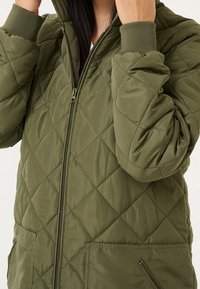 Olive green quilted jacket featuring a zip front, elastic cuffs, and side pockets. Soft, smooth fabric with diamond pattern stitches.