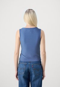 Top sans manches à côtes dans une teinte bleu dégradé, associé à un jean bleu avec poches arrière et détail de logo. Texture lisse.