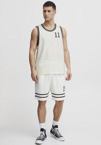 Hvit mesh basketballtrøye med svarte detaljer, med nummer 11. Kombinert med hvite shorts, også accentuert med svarte striper. Svarte joggesko.
