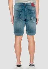 Denim kratke hlače svetlo modre barve s zvitimi robovi, pet žepov in maroon usnjenim oznako na zadnjem pasu. Obuta ima bele športne čevlje.